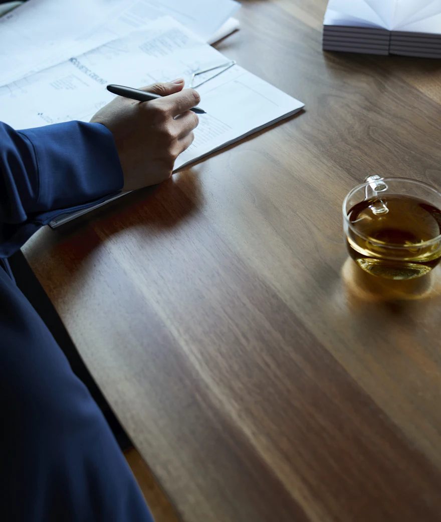 A hand marking up a document on a wooden desk